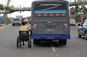 Un minusválido en silla de ruedas se desplaza agarrado de una guagua en la avenida Gómez esquina Kennedy - 