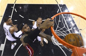 El delantero de los Miami Heat, LeBron James, anota con fortaleza dos puntos ante la defensa de Tim Duncan, de San Antonio Spurs, y su compañero Kawhi Leonard, anoche en el AT&T Center en San Antonio, Texas. Miami empató la serie final de la NBA 1-1.